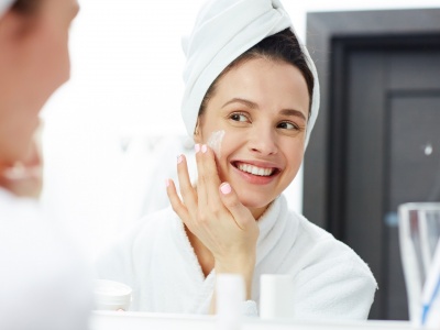 Perfect young woman applying facial cream in bathroom
